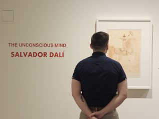 Person standing looking at print with text "The Unconscious Mind: Salvador Dali" on the wall